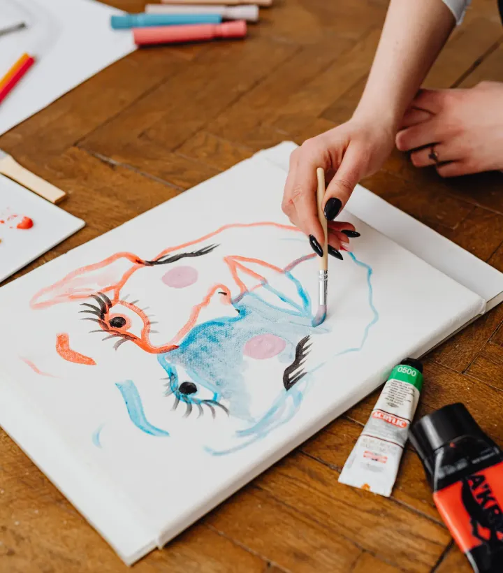 A person painting on canvas with art materials spread across a table